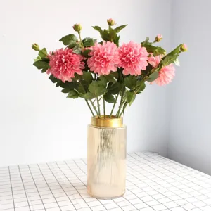 Gros plan détaillé d'un bouquet de dahlias roses artificiels dans un vase cannelé doré.