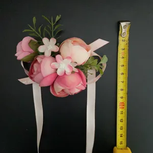 Artificial pink rose wrist flower wedding corsage with green leaves and ribbon detail.