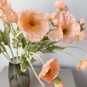 Detailed closeup of coral pink artificial Iceland poppy flowers with velvet texture in glass vase.