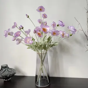 Close-up detail of artificial light purple Icelandic poppy flowers in a sleek clear glass vase.
