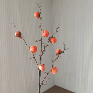 Détail de branche de kaki artificiel avec petits fruits orange pour la décoration intérieure.