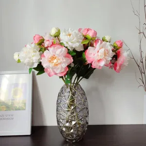 Detailed scene of artificial peony and ranunculus flower bouquet in modern glass vase home decor.