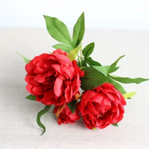 Close-up detail of artificial red peony flowers with green leaves for home decor and display.