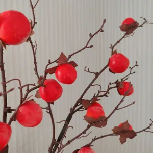 Détail de branche de kaki artificielle, faux fruit rouge pour déco, accessoire gros plan.