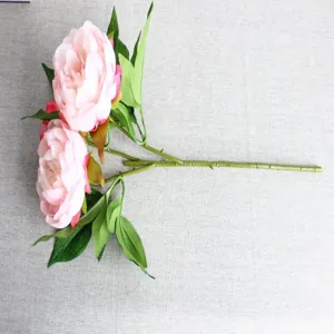 Detailed view of artificial pink peony flower branch with realistic green leaves and stem.