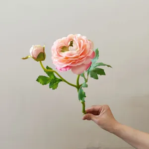 Artificial camellia flower detail, pink silk floral branch with bud and green leaves close up.