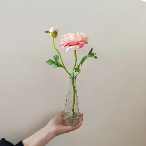 Detailed close-up of pink artificial camellia flower with glass vase for home decor.