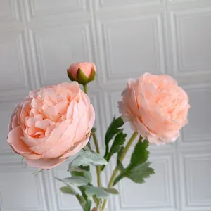 Primo piano dettagliato di fiori artificiali di ranuncolo pesca con tre teste e foglie.