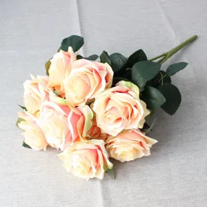 Close-up detail of artificial rose bouquet showing soft pink gradient petals and green leaves on fabric.