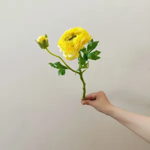 Artificial flower detail shot showing yellow ranunculus bloom and green leaf stem clearly.