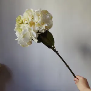 Close up detail of artificial white hydrangea flower stem held by hand for home decor display.