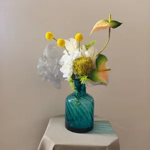 Gros plan sur un bouquet de fleurs artificielles dans un vase en verre torsadé bleu décoration.
