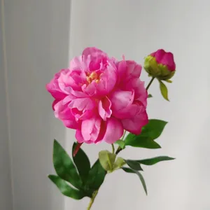 Detailed close-up of a vibrant pink artificial peony flower branch with lush green leaves.