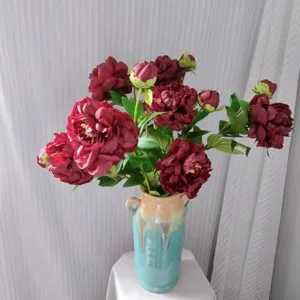 Detailed close-up of artificial red peony bouquet in ceramic vase, elegant floral home decor.