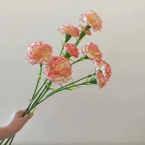 Detailed close-up of artificial carnation flowers with realistic pink-edged petals and green stems.