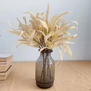 Vue rapprochée d'un bouquet d'eucalyptus artificiel avec baies dans un vase en verre.