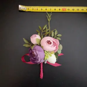 Botonier de flores artificiales en rosa y morado con hojas verdes y cinta para boda.