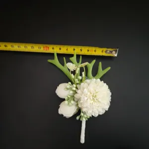 White artificial boutonniere wedding groom corsage with green leaves detail view