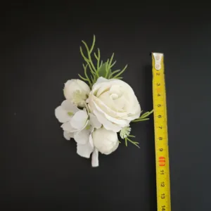 Detailed view of white artificial rose boutonniere with green filler leaves and size measuring tape.