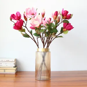 Nahaufnahme künstlicher Magnolienblüten in gerippter Glasvase mit Goldrand für Heimdekoration.