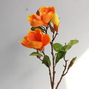 Nahaufnahme des künstlichen orangefarbenen Magnolienzweigs mit Blüten und grünen Blättern.