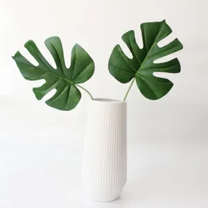 Primo piano di foglie di monstera artificiali in un vaso di ceramica bianca decorativo.