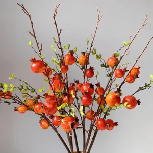 Dettaglio ramo di melograno artificiale con frutti rossi e foglie verdi per decorazione casa.