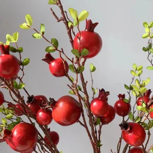 Dettaglio ramo di melograno finto con frutti rossi realistici e foglie verdi per decoro.