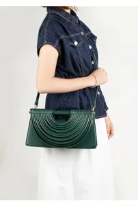 Detail shot of the elegant dark green pleated crossbody bag worn by a model, showing texture.