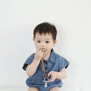 Baby pacifier clip detail showing wooden fastener and silicone connector worn by infant.