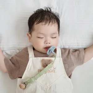 Detail view of baby silicone pacifier clip chain with cute bear romper in sleeping scene.