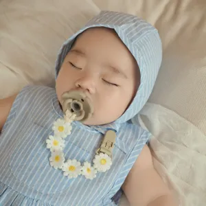 Close-up of cute baby sleeping with sweet daisy pacifier clip chain accessory detail shot.
