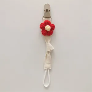 Close-up detail of handmade knitted flower pacifier clip with secure plastic clip and strap.