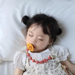 Nahaufnahme des süßen Babyschnuller-Clips aus Silikon mit Perlen auf weicher weißer Bettwäsche.