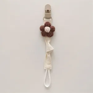 Close-up detail of a handmade knitted flower baby pacifier clip with secure fabric strap.