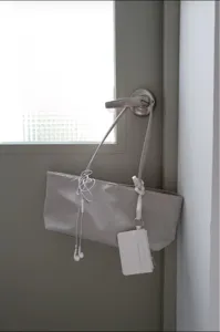 Detail view of minimalist grey tote bag hanging on a door with a white card pouch and earphones.