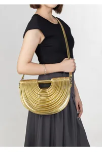 Detail view of a unique metallic gold pleated semicircle shoulder bag worn by a model in studio
