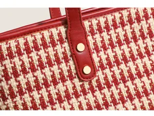Close-up detail of red and beige houndstooth tote bag fabric texture and leather strap.
