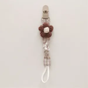 Detail view of handmade knitted flower pacifier clip with plaid fabric and clip.