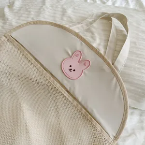 Hanging mesh storage bag detail, cute rabbit patch, bathroom toy organizer, beige color.
