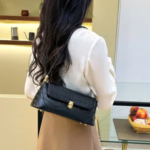 Detailed shot of a stylish black crocodile embossed baguette shoulder bag worn by a model indoors.