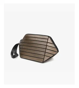 Bronze geometric clutch bag detail showing unique striped texture, black wrist strap, and zipper.