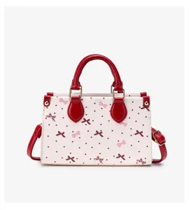 Close-up view of women's PU leather handbag featuring polka dot and bow print with red handles.