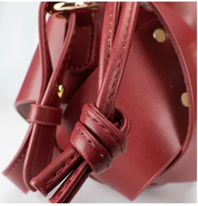 Wine red leather bucket bag featuring a chic knotted strap and refined stitching detail.