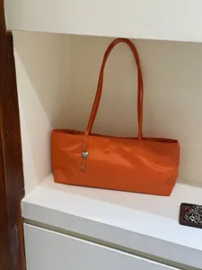 Lightweight orange nylon shoulder tote bag with minimalist design and chic key charm accessory.