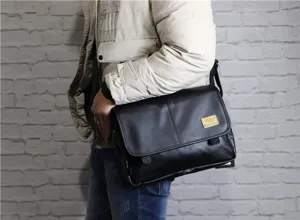 Detailed shot of black PU leather messenger bag worn crossbody by model against brick wall.