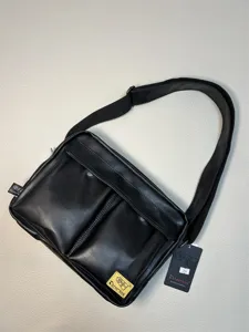 Black PU leather messenger bag detail, featuring dual front pockets and adjustable strap.