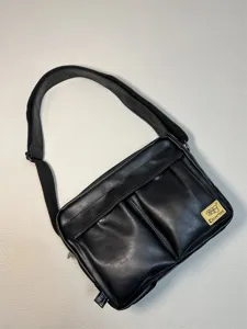 Black PU leather messenger bag detail, featuring dual front pockets and adjustable strap.