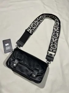 Close-up detail of the black retro crossbody bag with wide patterned strap and hardware.