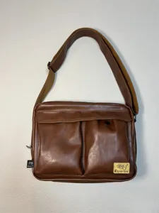 Detailed view of the brown leather messenger bag featuring dual front pockets and shoulder strap.